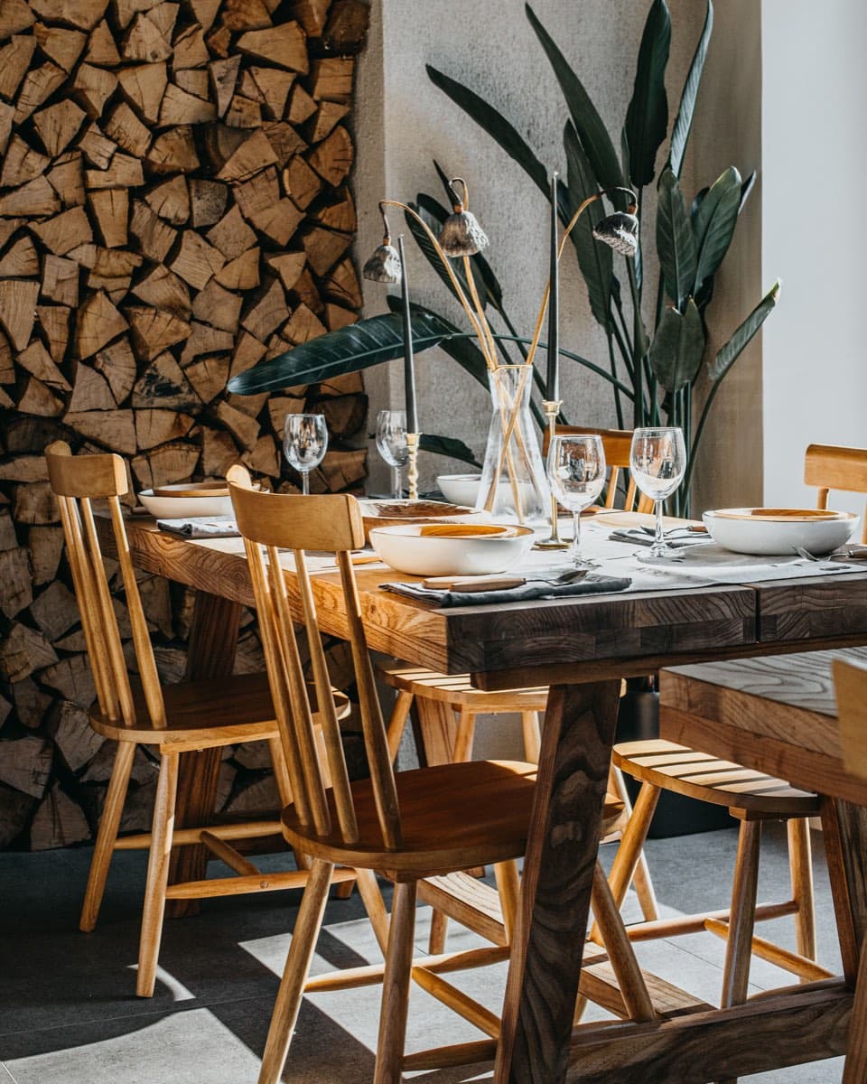 A timber dining table set beside a stacked log wall